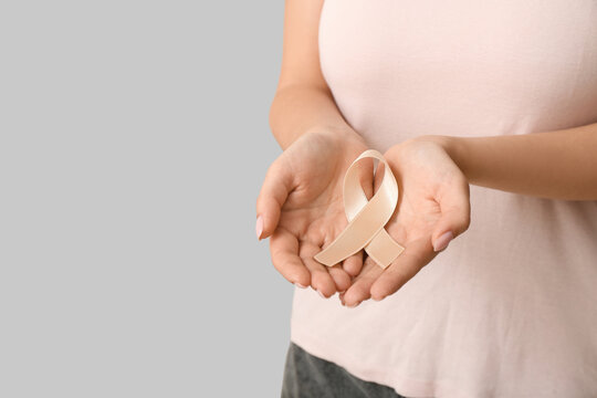 Woman with beige ribbon on light background, closeup. Uterine cancer awareness concept