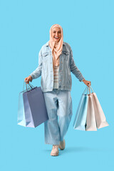 Stylish Muslim woman with shopping bags on blue background