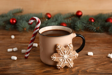 Cup of tasty Christmas cocoa with marshmallows, candy cane and cookie on wooden background