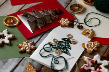 Concept of christmas craft, handmade presents, family leisure time, hobby, recreation. Flat lay, top view with paper postcard with new year fir tree made with recyclable materials. Gingerbread cookies