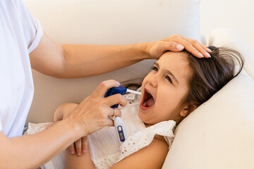 Mom treats her little daughter's cold and throat by spraying the medicine into the child's mouth....