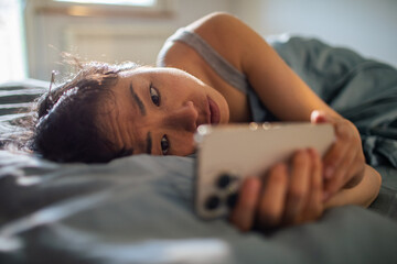 Young Asian woman using a smartphone after waking up in her bed at home