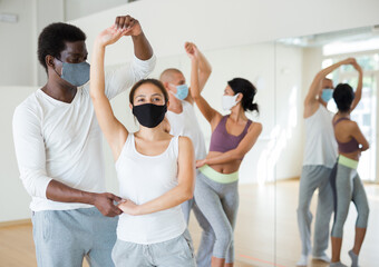 Young Hispanic woman and African American man in protective face masks learning to dance waltz...