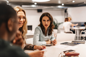 Beautiful, brunette, female employee looking confused while having misunderstanding with her male coworker.