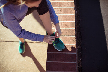 Young woman runner tying her sneakers on the sidewalk