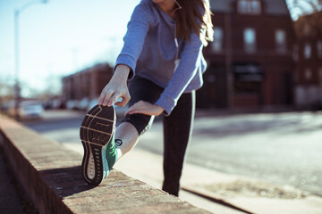 Sporty young woman stretching her legs before a run in the city