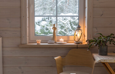 Scandinavian-style room in white wooden house, winter outside. Angel, candles, lantern on windowsill