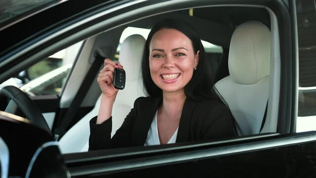 Happy beautiful lady sitting in her new car and showing the keys. Transport, trip, lifestyle concept. Slow motion