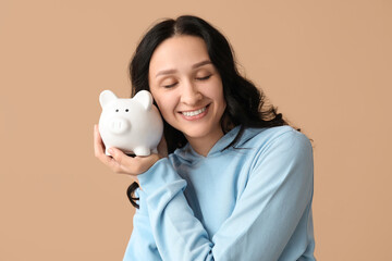Pretty young woman with piggy bank on beige background