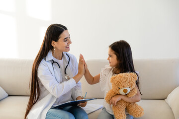 Doctor visit sick child at home. Pediatrician meets little patient during home visit, girl sits on coach, gives high five to doctor, medical care, shows warm attitude towards child concept.