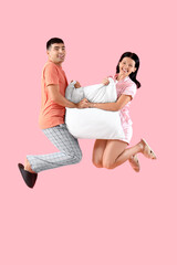 Fototapeta na wymiar Young couple with pillow jumping on pink background