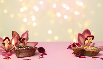 Diya lamps with orchid flowers on pink table against blurred lights. Divaly celebration