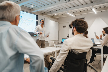 Multiracial, inter-generational group of businesspeople listening to a middle-aged, experienced male teacher sharing knowledge and business guidance