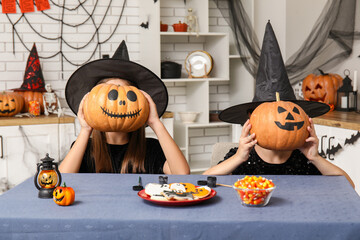 Cute little girls dressed for Halloween as witches with candies and pumpkins at table in kitchen