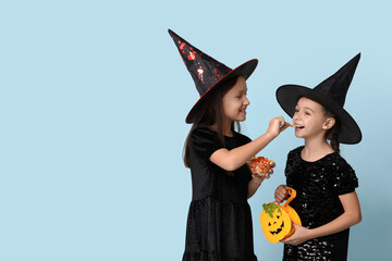 Cute little girls dressed for Halloween as witches with bag and bowl of candies on blue background