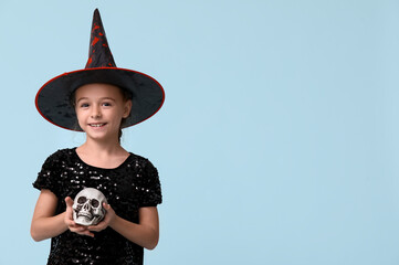 Cute little girl dressed for Halloween as witch with human skull on blue background