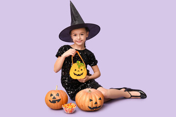 Cute little girl dressed for Halloween as witch with pumpkins, bag and candies sitting on purple background