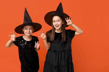Cute little girls dressed for Halloween as witches on orange background