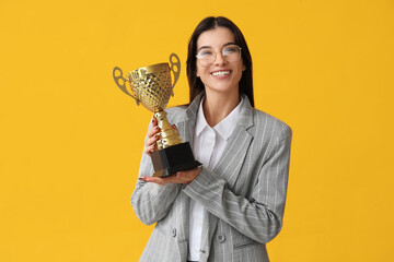 Young businesswoman with gold cup on yellow background
