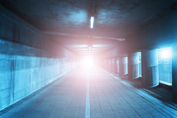Horror tunnel background. Dark pavement tunnel with bright light at the end. Scary walkway under the bridge. Grunge urban bridge construction. Bright spot light at the end of a tunnel.