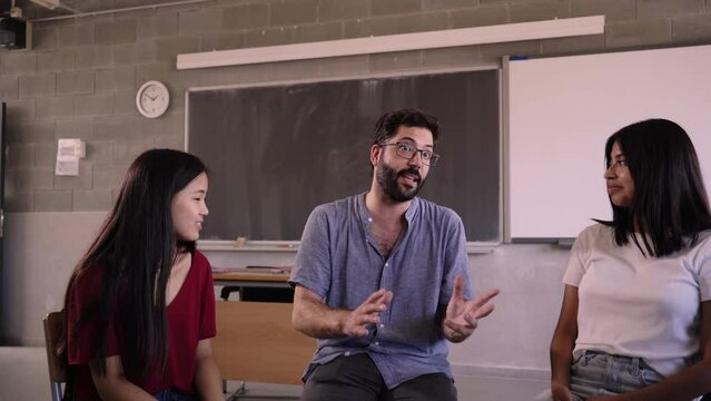 High school teacher discusses concepts from course syllabus with students. Classmates in shared classroom at an international school. Multiracial young people learning new concepts at university.