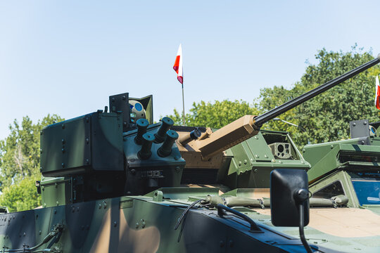 The upper part of military tank covered in camouflage paint with a white and red Polish flag on the top. Blue sky and green trees in the background. High quality photo