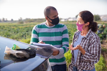 Courier in protective mask invites the farmer to sign documents on the farmer field