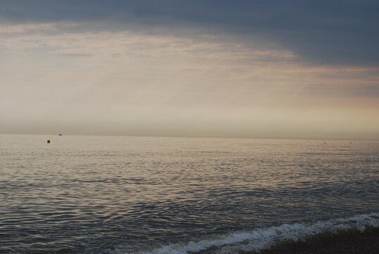 Gentle Atlantic Ocean Sea Ebbing and Flowing on Smooth Natural Stone Pebble Beach in England with Misty Stormy Horizon with Setting Sun Casting Pinks Oranges Peeking Through Stormfront Warm Tones