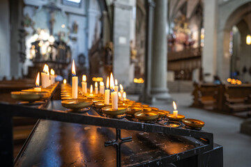 Tea lights burn in the left aisle of a bright Romanesque three-nave columned basilica. Minster...