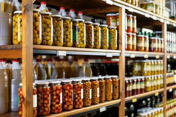Marinated whole unpitted green olives in glass jars offered for sale on shelf rack in store....