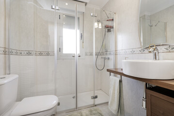 Tiled bathroom with white tiles, shower cabin with glass screens and circular porcelain sink with mirror on the wall