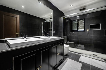 Black slate tiled bathroom with large glass-enclosed shower cubicle, black wooden cabinet, single...