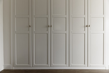 Front of a wardrobe with white wooden doors with golden metallic handles