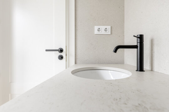 Image of the bathroom with cream tiles, matching countertop, matching black faucets with white door handle