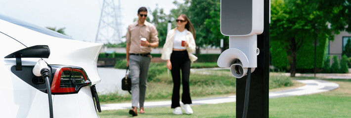 Young couple with coffee recharge EV car battery at charging station connect to electrical...