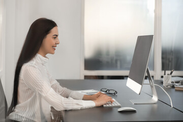 Fototapeta na wymiar Happy woman using modern computer at black desk in office