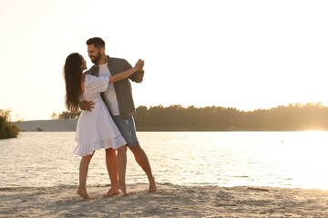 Happy couple dancing near river on sunny day. Space for text