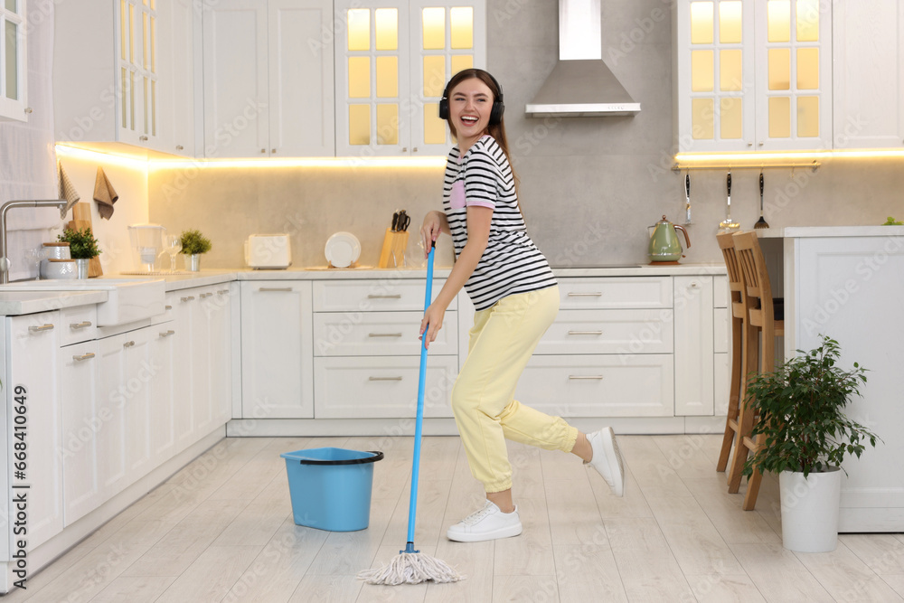 Sticker Enjoying cleaning. Happy woman in headphones dancing with mop in kitchen