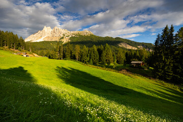 Wooden house stands amon picturesque summer nature in Dolomites. Small mountain settlement