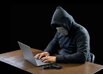 Hacker spy man one person in black hoodie sitting on a table looking computer laptop used login...