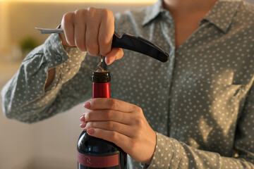 Woman opening wine bottle with corkscrew indoors, closeup
