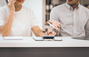 An older mature woman shows something to asian man on a laptop. They smile and work together in an office. They look happy and focused.