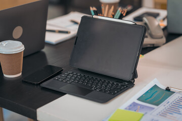 A laptop on a desk displays charts. There's a calculator, coffee, papers, and pens. The workspace...