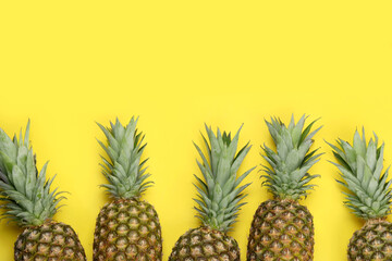 Fototapeta premium Whole ripe pineapples on yellow background, flat lay. Space for text