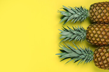 Whole ripe pineapples on yellow background, flat lay. Space for text
