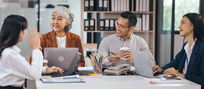 Four asian people in an office, working together on laptops, discussing tasks. annual gathering where attendees share and discuss opinions, presentation teamwork group meeting laptop in boardroom - Powered by Adobe