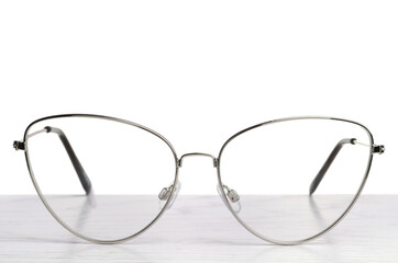 Stylish glasses with metal frame on wooden table against white background