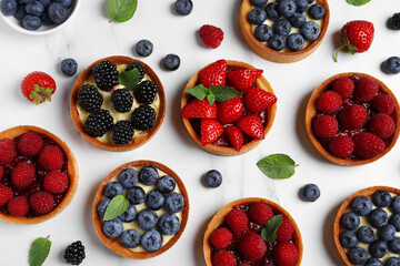 Tartlets with different fresh berries on white marble table, flat lay. Delicious dessert