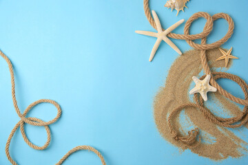 Fototapeta na wymiar Beautiful sea stars, rope and sand on light blue background, flat lay. Space for text