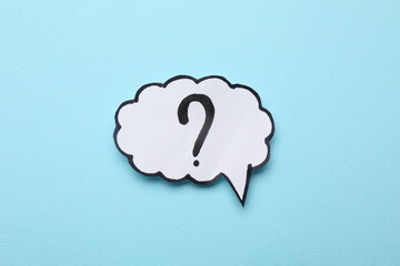 Paper speech bubble with question mark on light blue background, top view